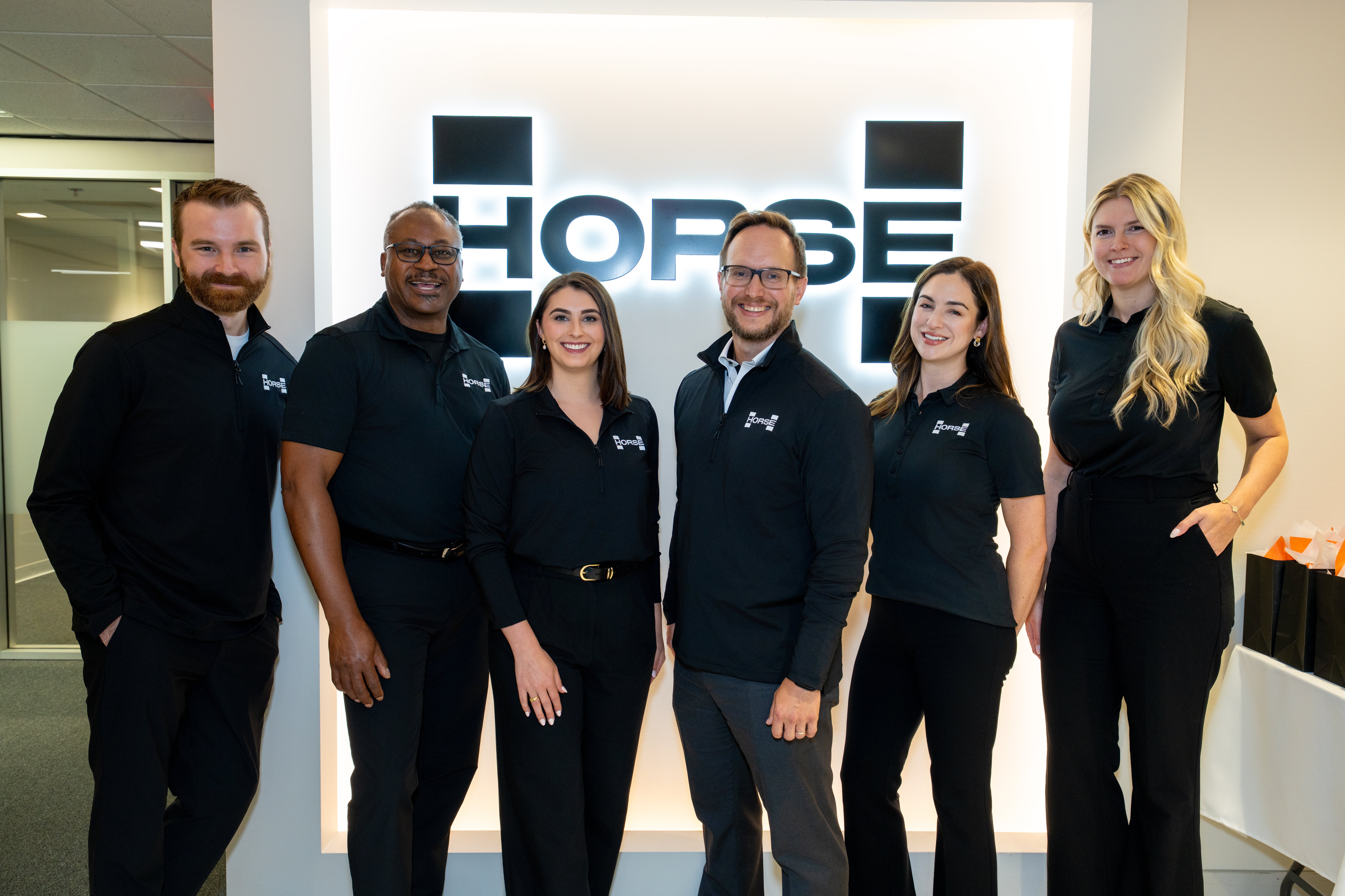 Six Horse Powertrain USA employees standing in a line in front of the company logo, wearing branded clothing