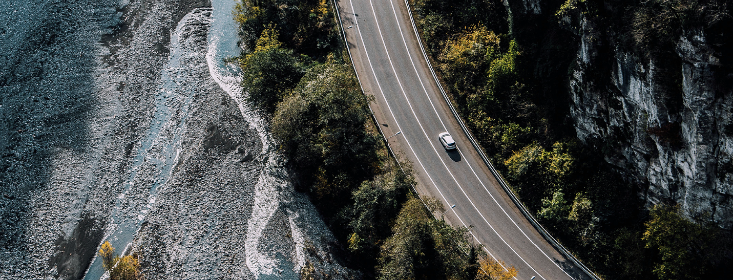 a white car on a country road with the ocean on the left side and the forest to the right 