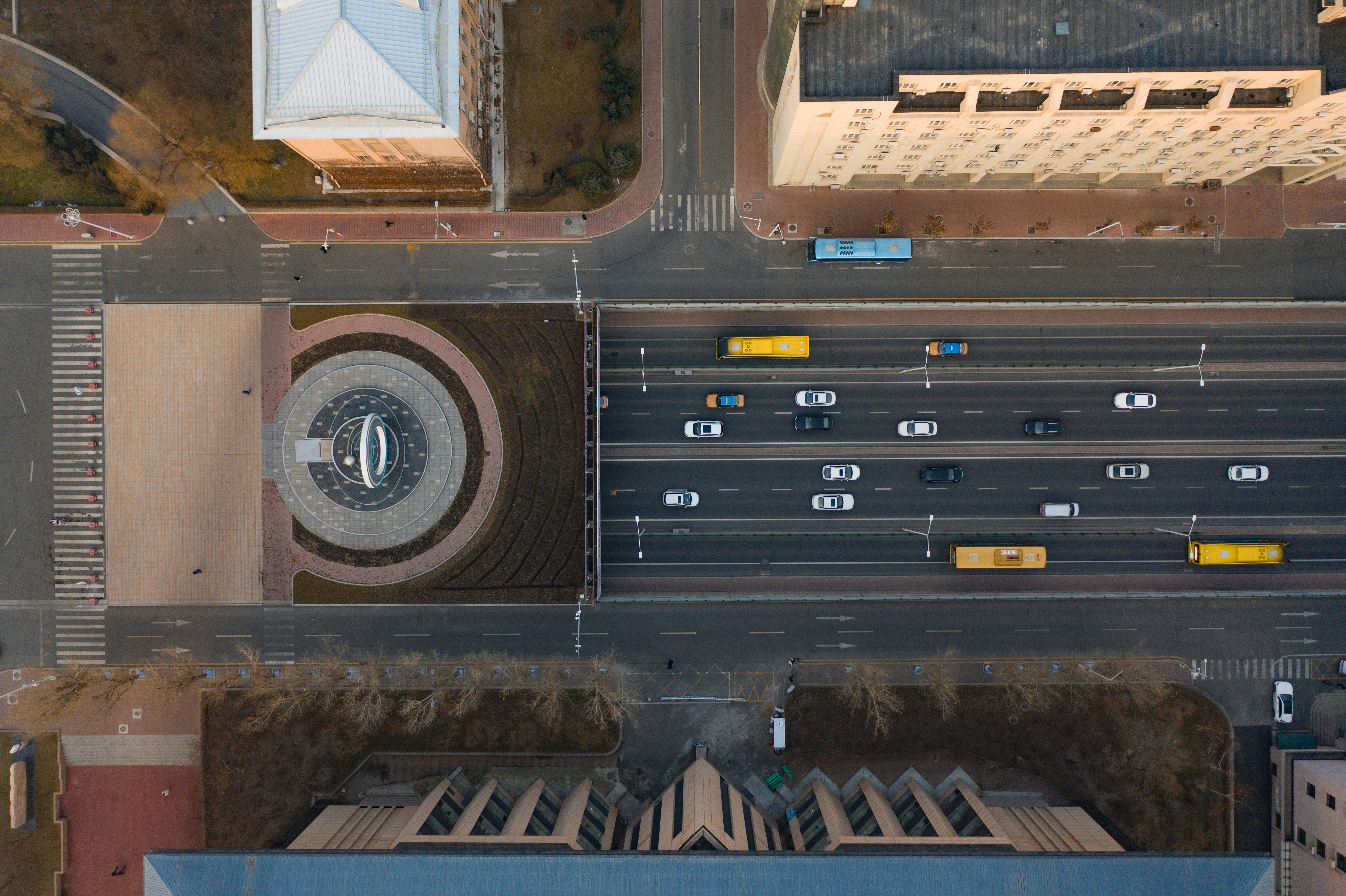 An aerial view of a cars on a city street heading into a tunnel, atop of which lies a circular statue