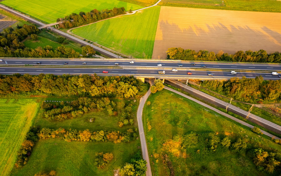 Several vehicles travelling on a motorway through a rural area above train tracks
