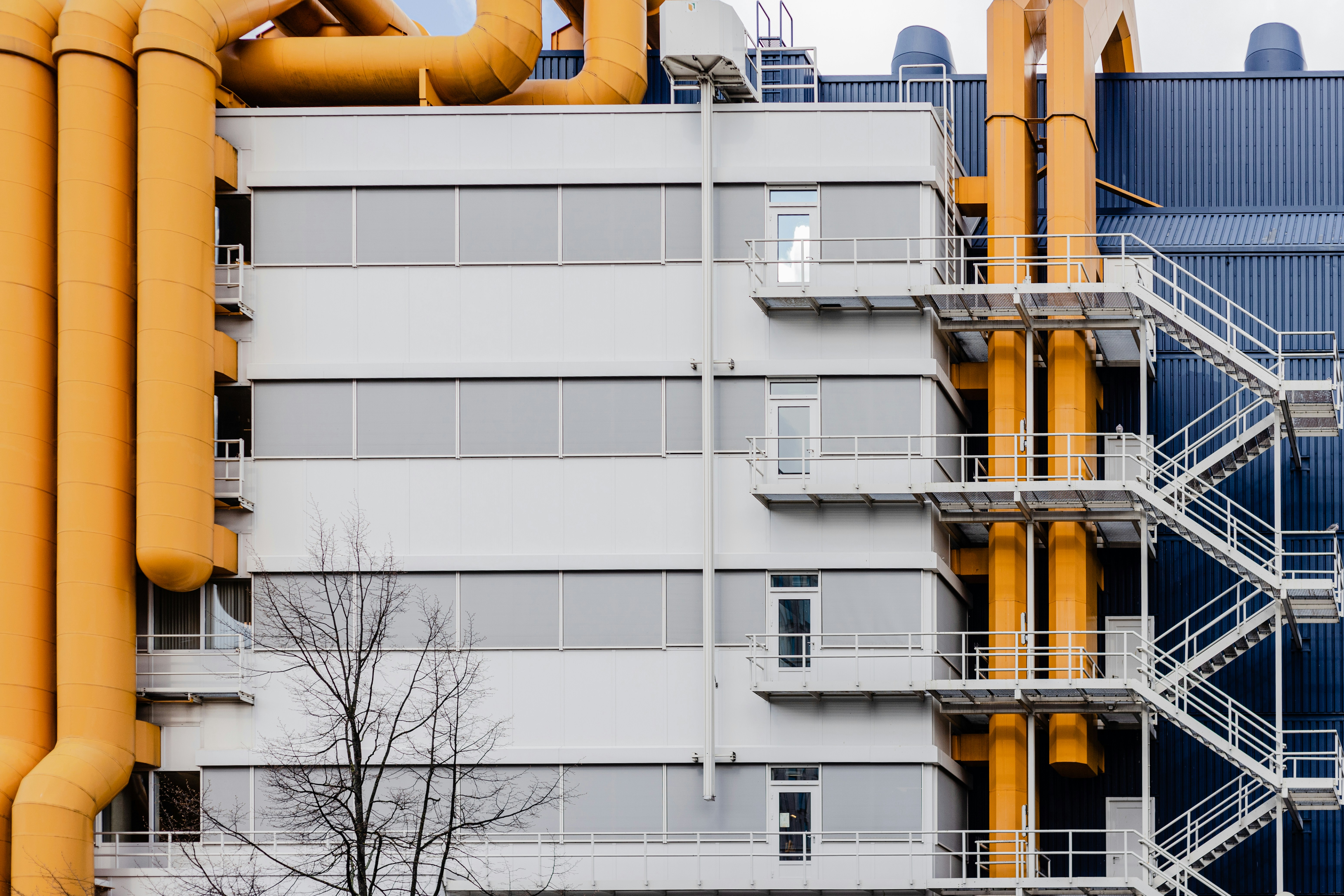 The side of an industrial building, featuring fire exit staircase and bright orange ventilation tubes