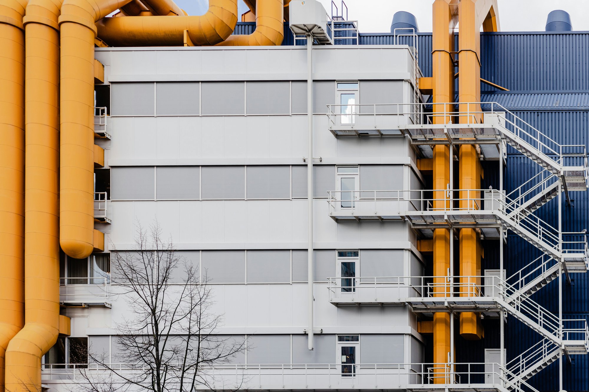 The side of an industrial building, featuring fire exit staircase and bright orange ventilation tubes